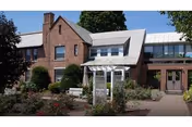 Brick senior living building facade with white arbor and landscaped walkway.
