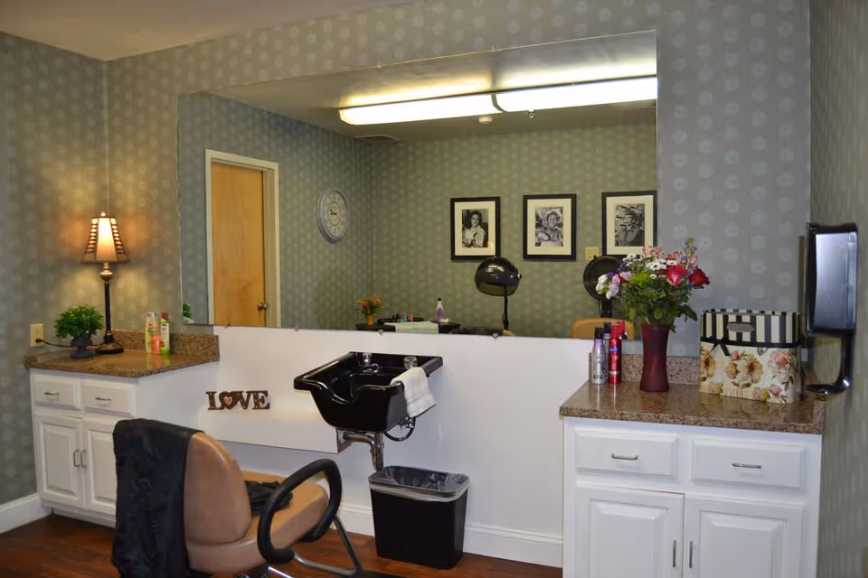 Interior salon station with a styling chair, black shampoo sink, large mirror, countertops and cabinets decorated with flowers and framed photos.