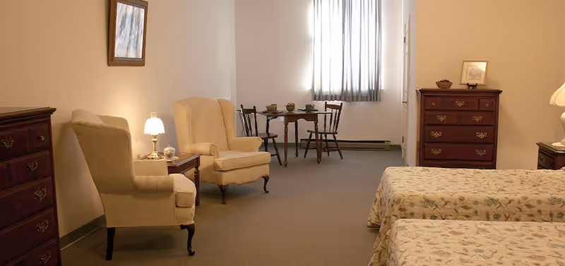 Large furnished bedroom with two twin beds, wingback chairs, dressers, and a small table and chairs by a window.