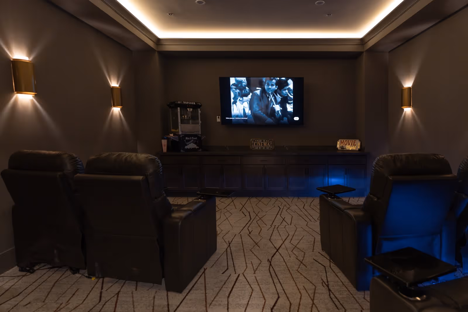 Dimly lit private theater room with leather recliners facing a wall-mounted TV and a snack station.