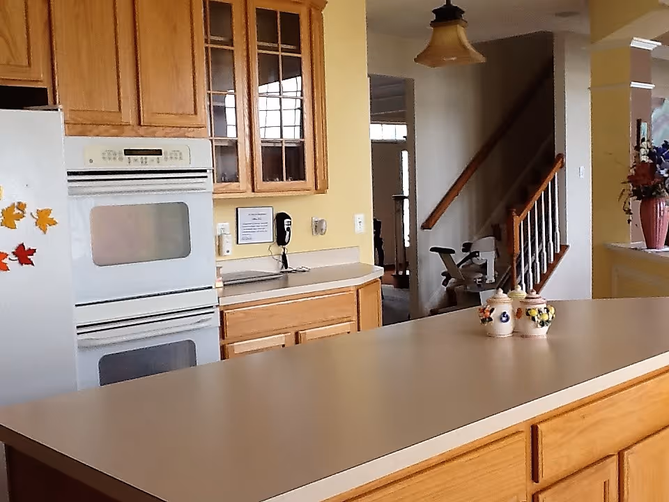 Kitchen with a long island countertop, wooden cabinets, double wall oven and a view toward a stairway.