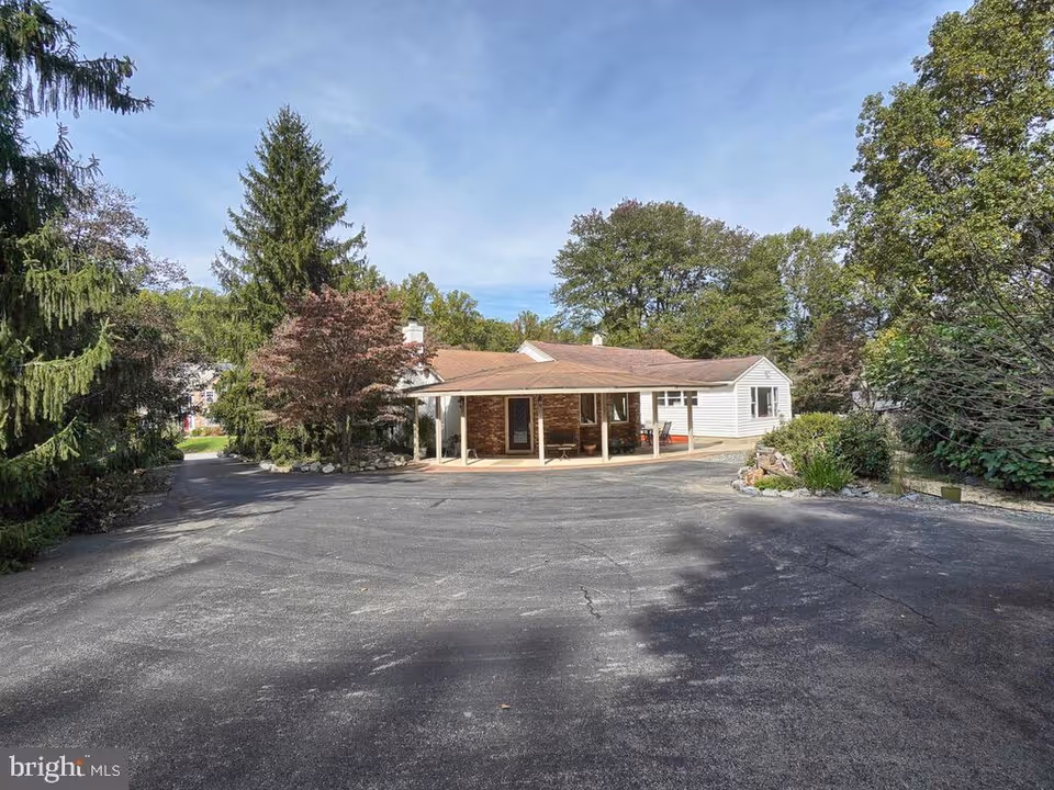 Single-story assisted living building with a covered front porch, surrounded by trees and a large paved driveway.