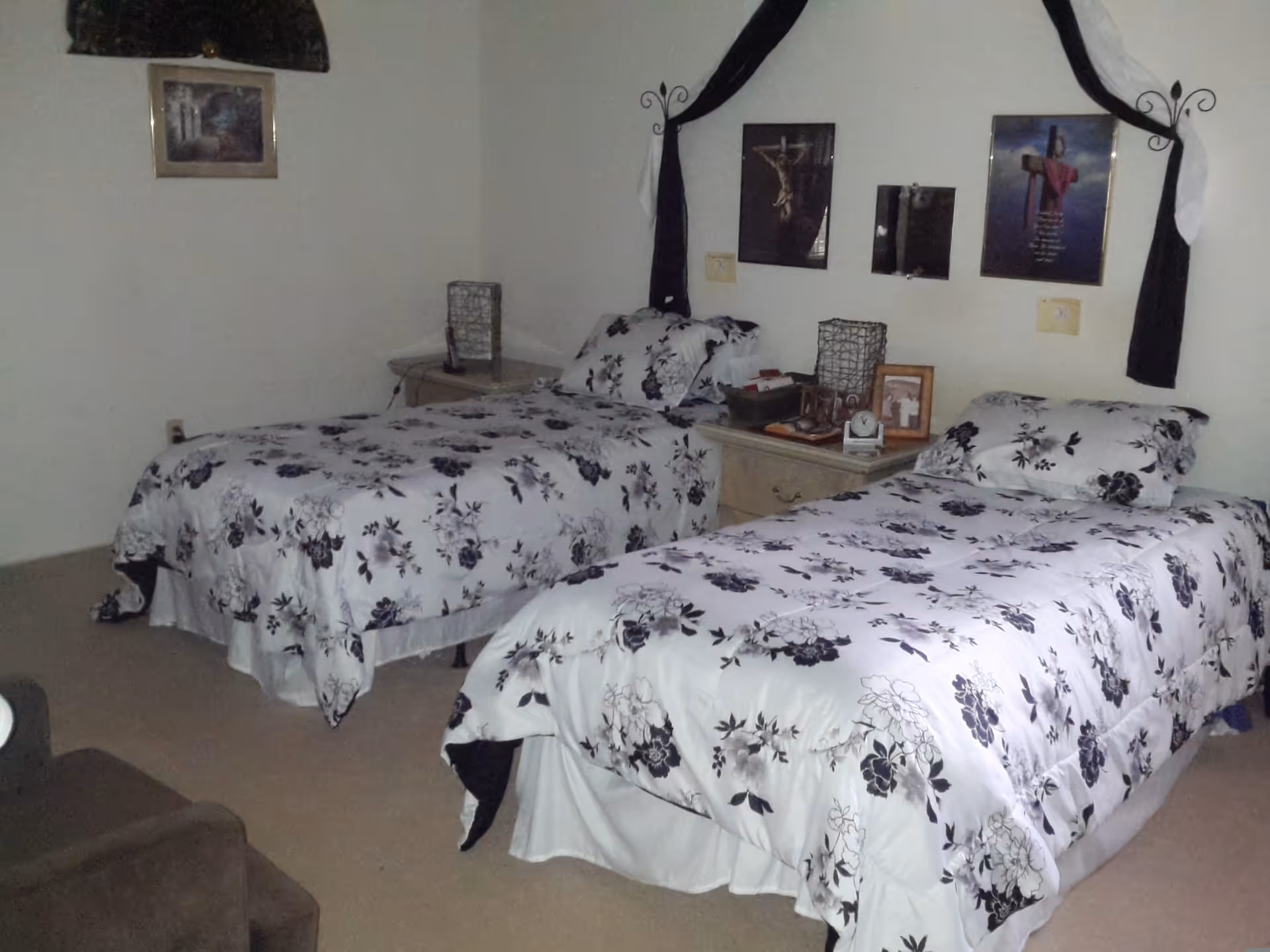 Two twin beds with matching white-and-black floral bedspreads and a shared nightstand in a simple bedroom.