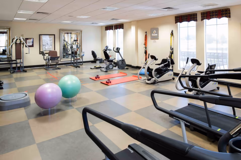 Bright exercise room with treadmills, recumbent bikes, exercise balls, mats, and strength equipment.