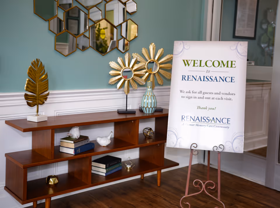 A decorative console table with books and ornaments next to a freestanding "Welcome to Renaissance" sign in a facility lobby.