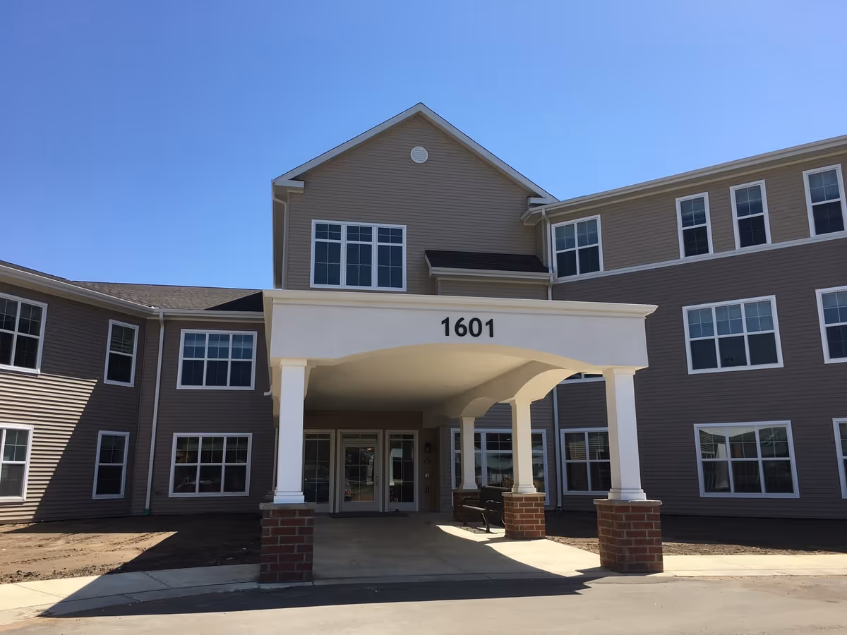 Front entrance of a multi-story beige senior living building with a covered portico displaying the number 1601.