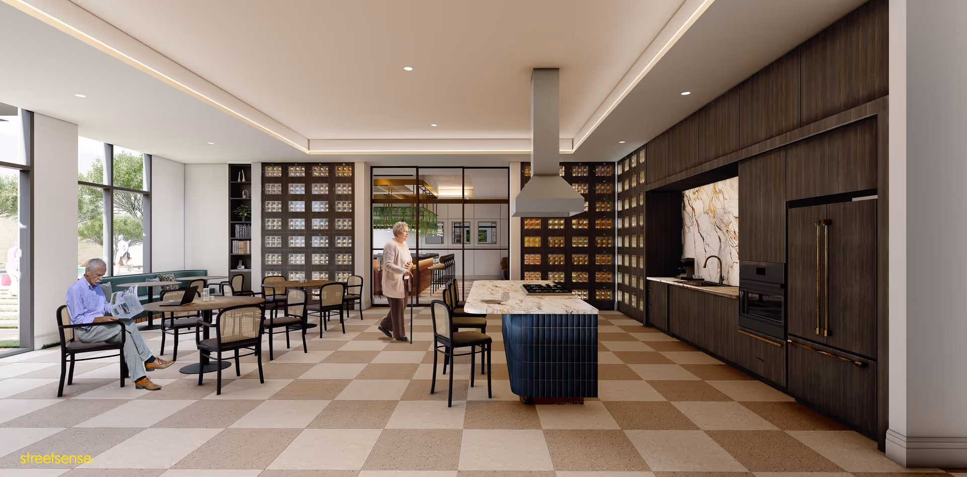 A modern communal kitchen and dining area in a senior living facility. The space features a large kitchen island with a marble countertop and a stove, surrounded by chairs. There are multiple dining tables with chairs, large windows letting in natural light, and a wall with built-in shelves and cabinets. An elderly man is seated reading a newspaper, and an elderly woman with a cane is standing nearby. Outside the windows, greenery and people walking are visible.