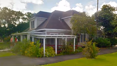 Front exterior view of The Dugger House Inc. senior living home with porch and greenery.