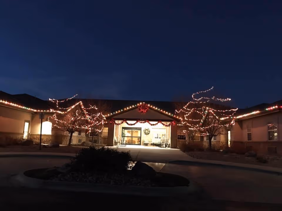 Front entrance of a senior living facility decorated with holiday lights and wreaths at dusk.