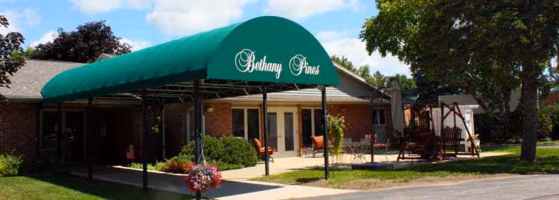 Exterior view of Bethany Pines with a green awning, brick building, and outdoor seating.