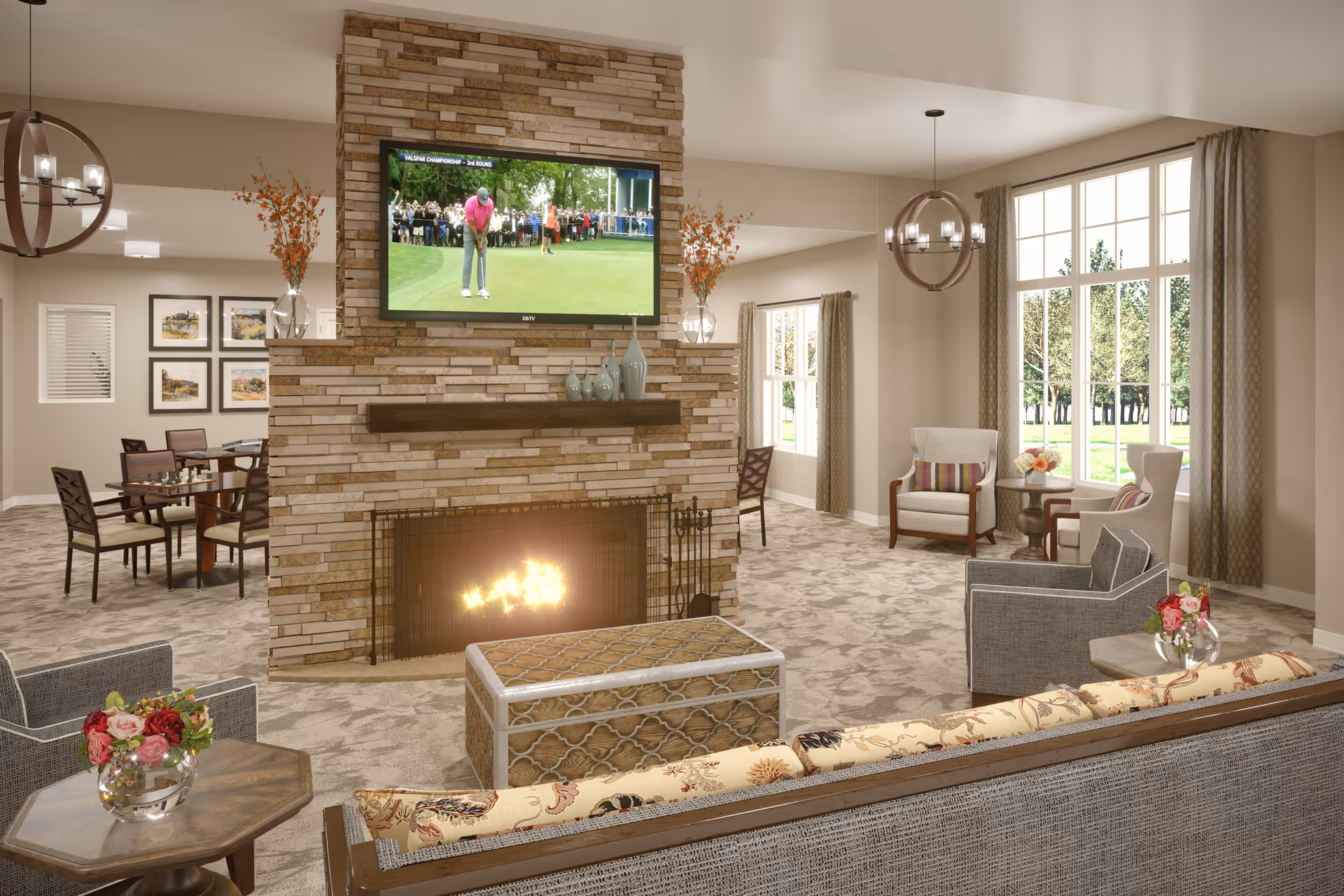 A cozy living room area in a senior living facility with a stone fireplace and a flat-screen TV mounted above it showing a golf game. The room features comfortable seating including armchairs and a sofa with floral cushions, a wooden coffee table, and side tables with flower vases. Large windows with curtains allow natural light to fill the space, and a dining area with tables and chairs is visible in the background.