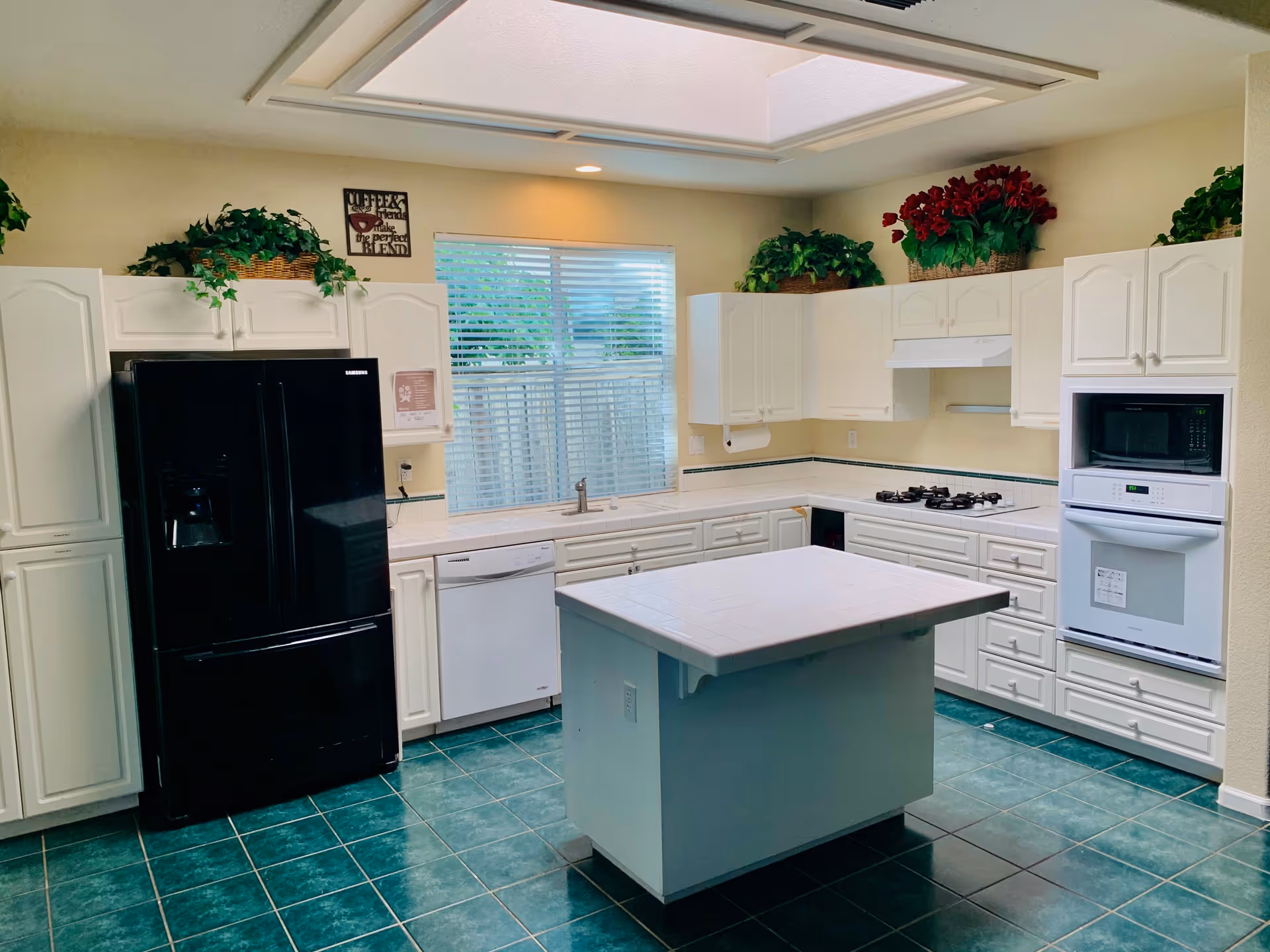 Bright kitchen with white cabinets, a central island, black refrigerator, built-in oven and microwave, and green tiled floor.