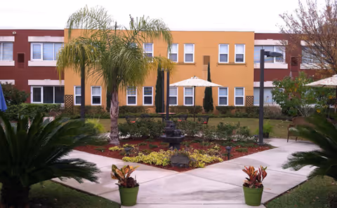 Courtyard with walkways, landscaped garden, palm trees and a central fountain in front of a two-story building.