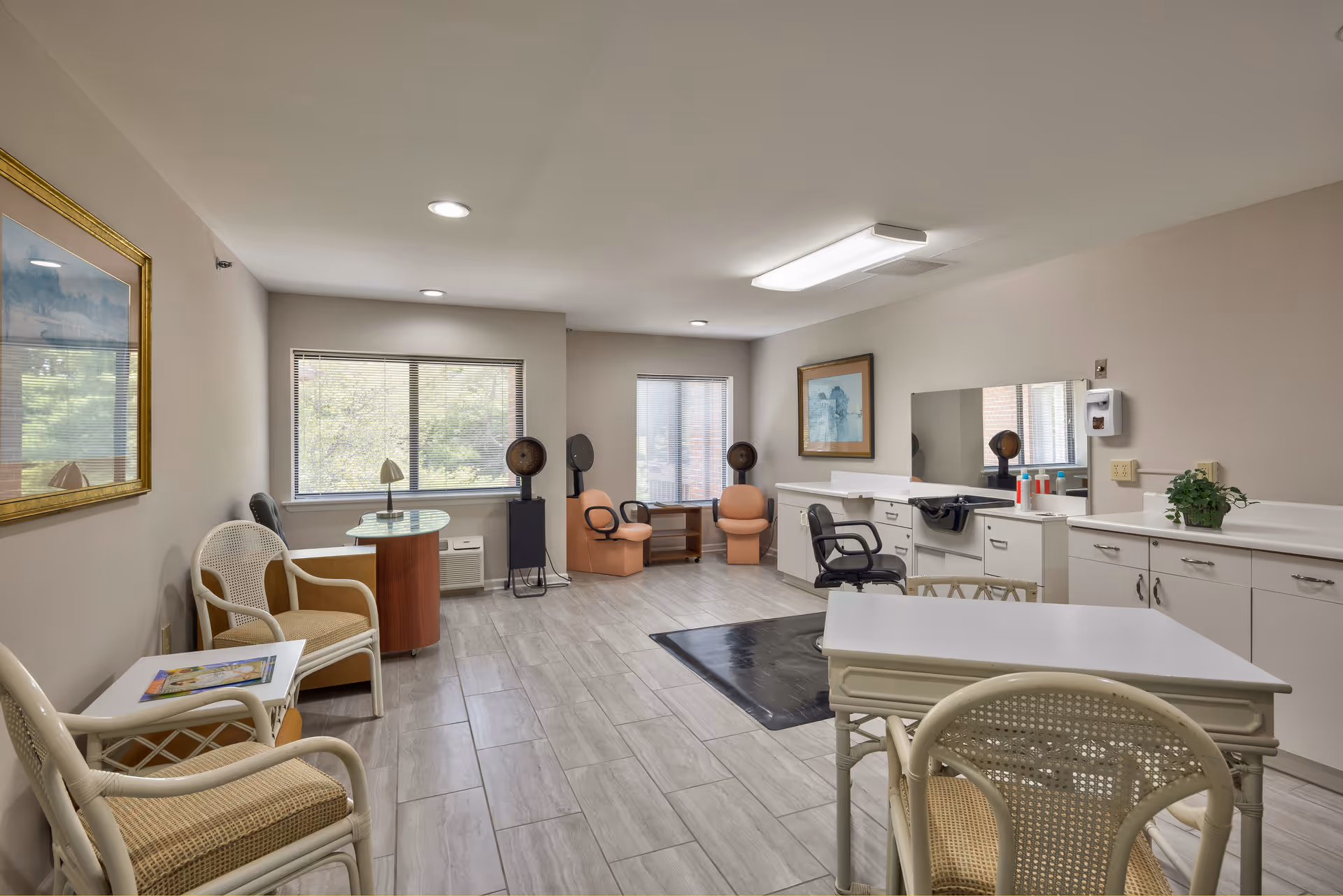 Bright salon-style common room with styling stations, chairs, sinks, and tables.