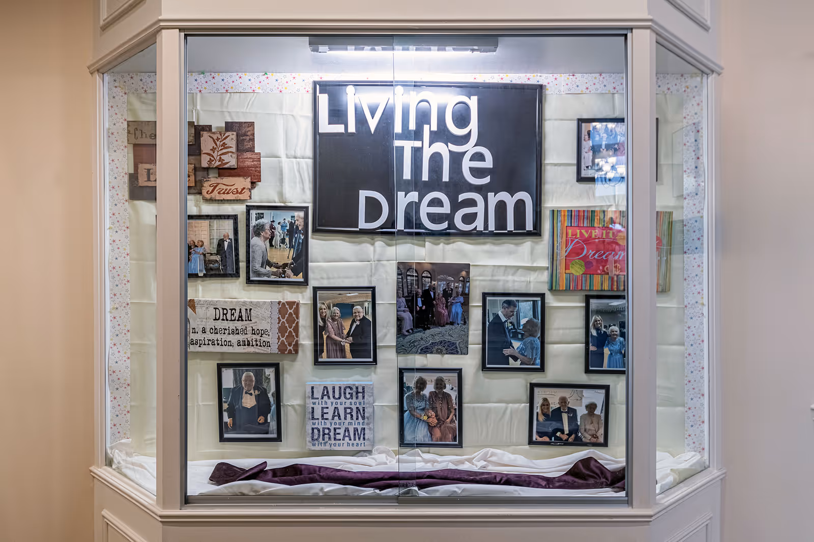 Glass display case inside a senior living facility showcasing framed photos and signs with the message "Living The Dream."