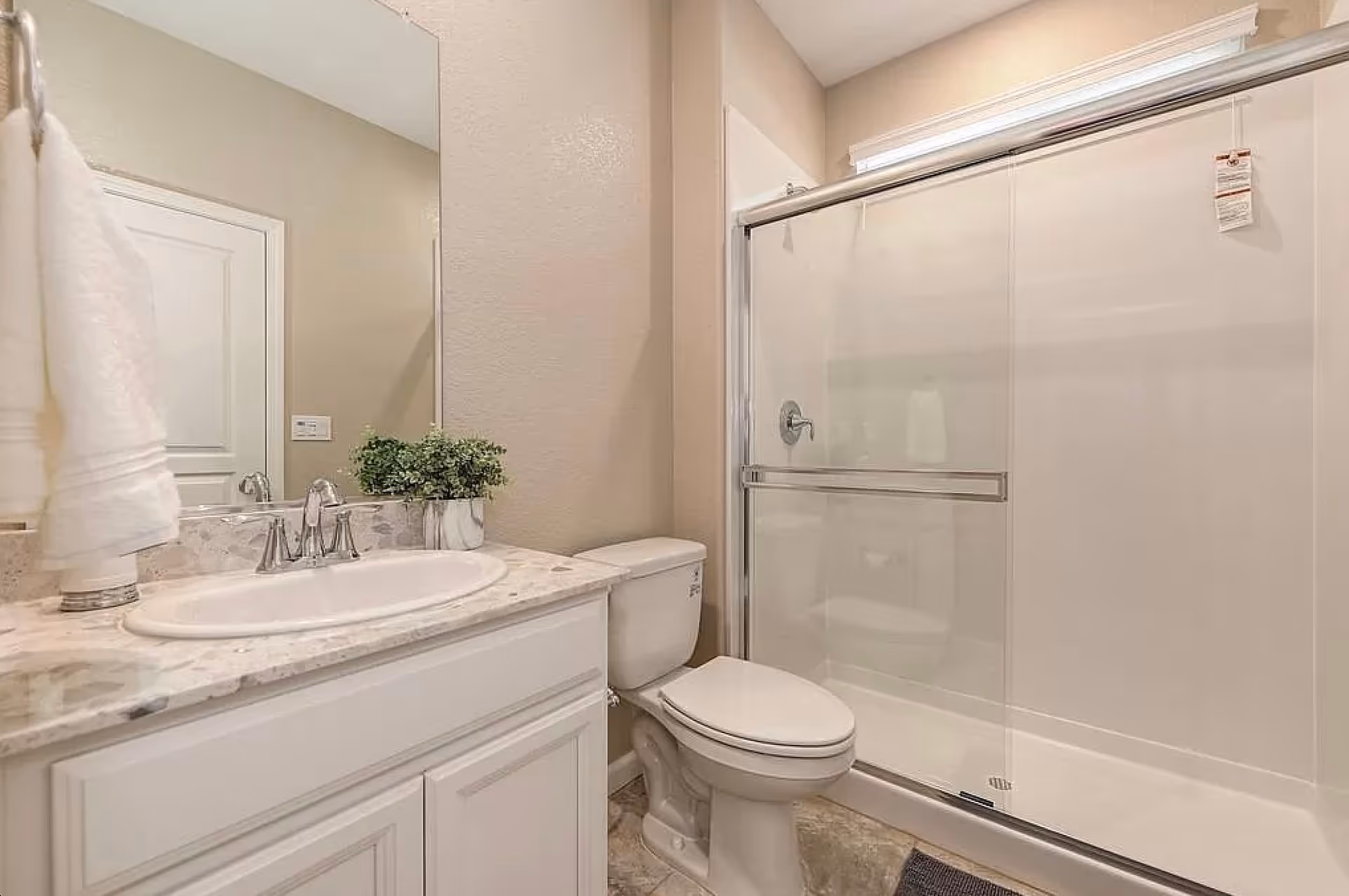 Bright bathroom with a sink vanity, toilet, and a glass-enclosed shower.