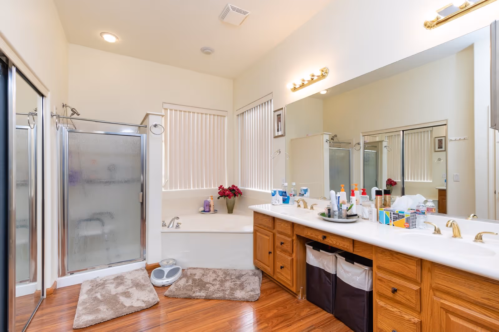 Well-lit spacious bathroom with a double-sink wooden vanity and large mirror, a corner shower, and a bathtub.