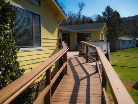 Wooden ramp to yellow senior living facility entrance with green lawn.