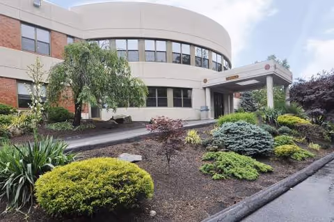 Curved beige building exterior with landscaped front garden and accessible entrance canopy.