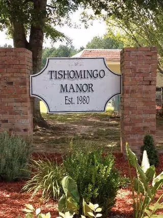 Tishomingo Manor entrance sign between brick pillars with landscaping