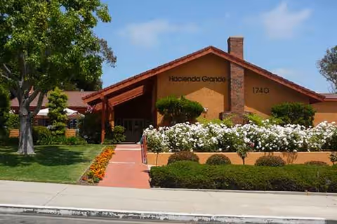 Front view of Hacienda Grande Senior Assisted Living with a brick entrance, walkway, and blooming shrubs.