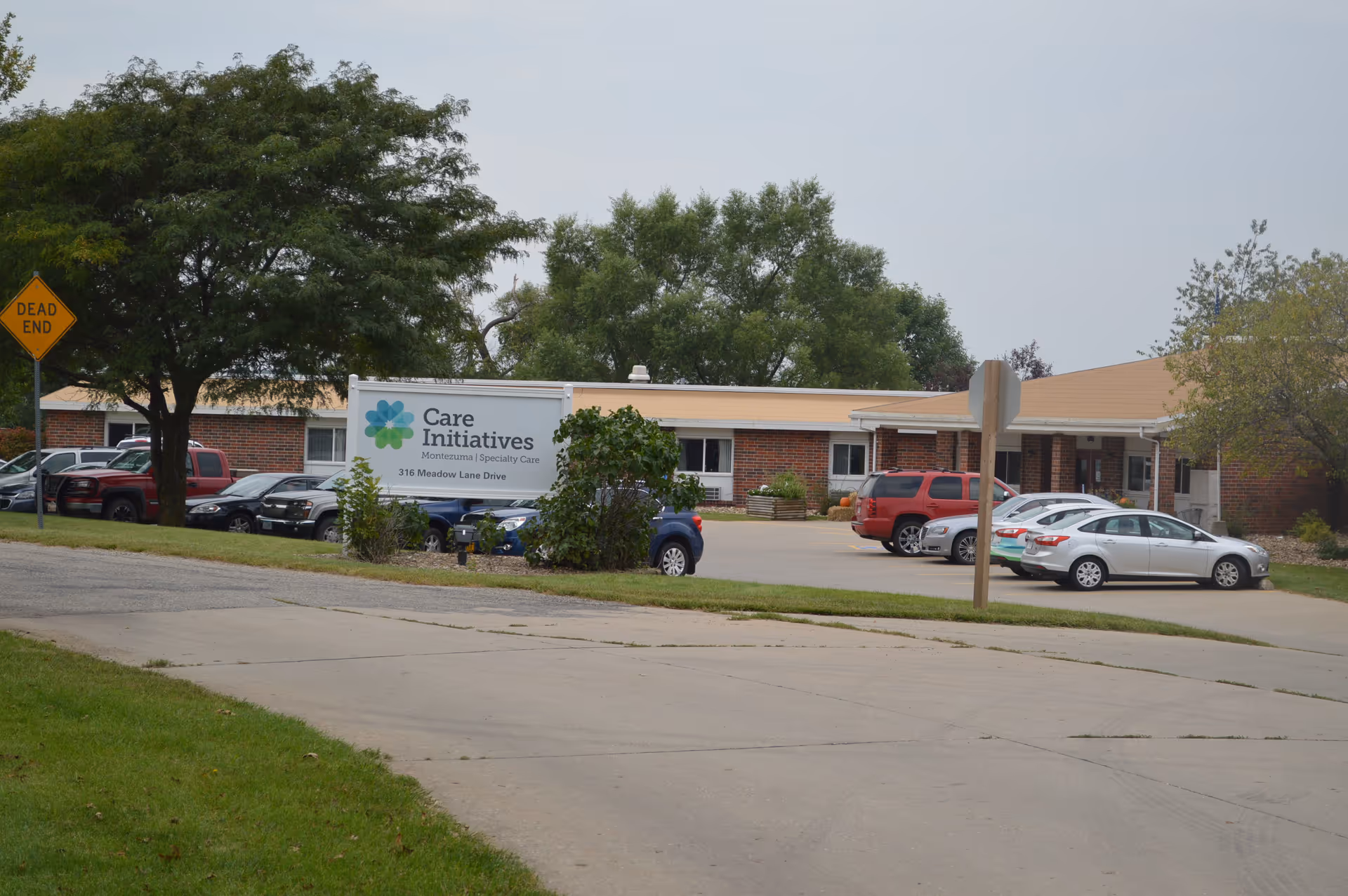 Single-story brick senior care facility building and parking lot with a 'Care Initiatives — Montezuma Specialty Care' sign in front.