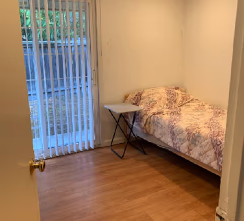 A small bedroom with a single bed, quilt, nightstand, and sliding door with blinds.