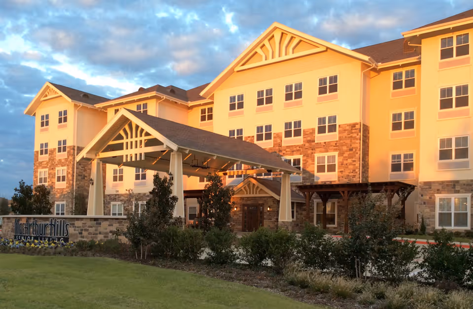 Front entrance of a multi-story senior living building with a covered porte-cochère and landscaped foreground.