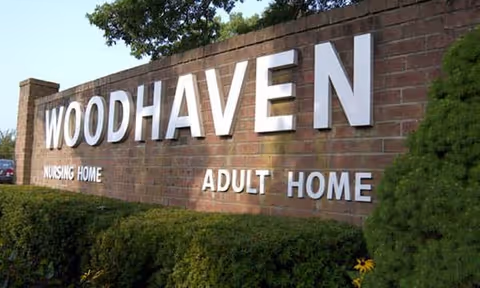 Exterior brick sign reading WOODHAVEN Nursing Home with surrounding shrubs.