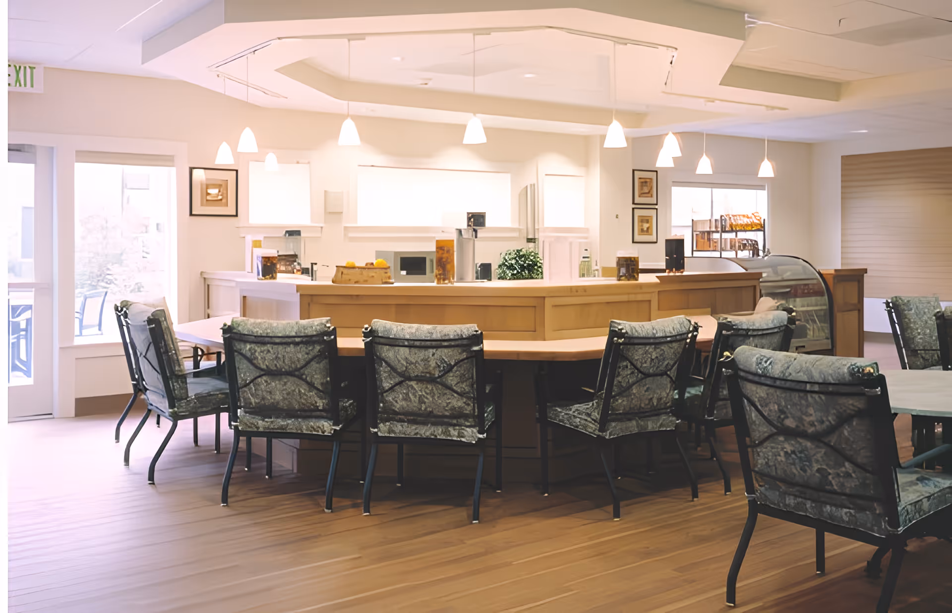 Well-lit communal dining area with a curved serving counter surrounded by cushioned chairs and pendant lights.