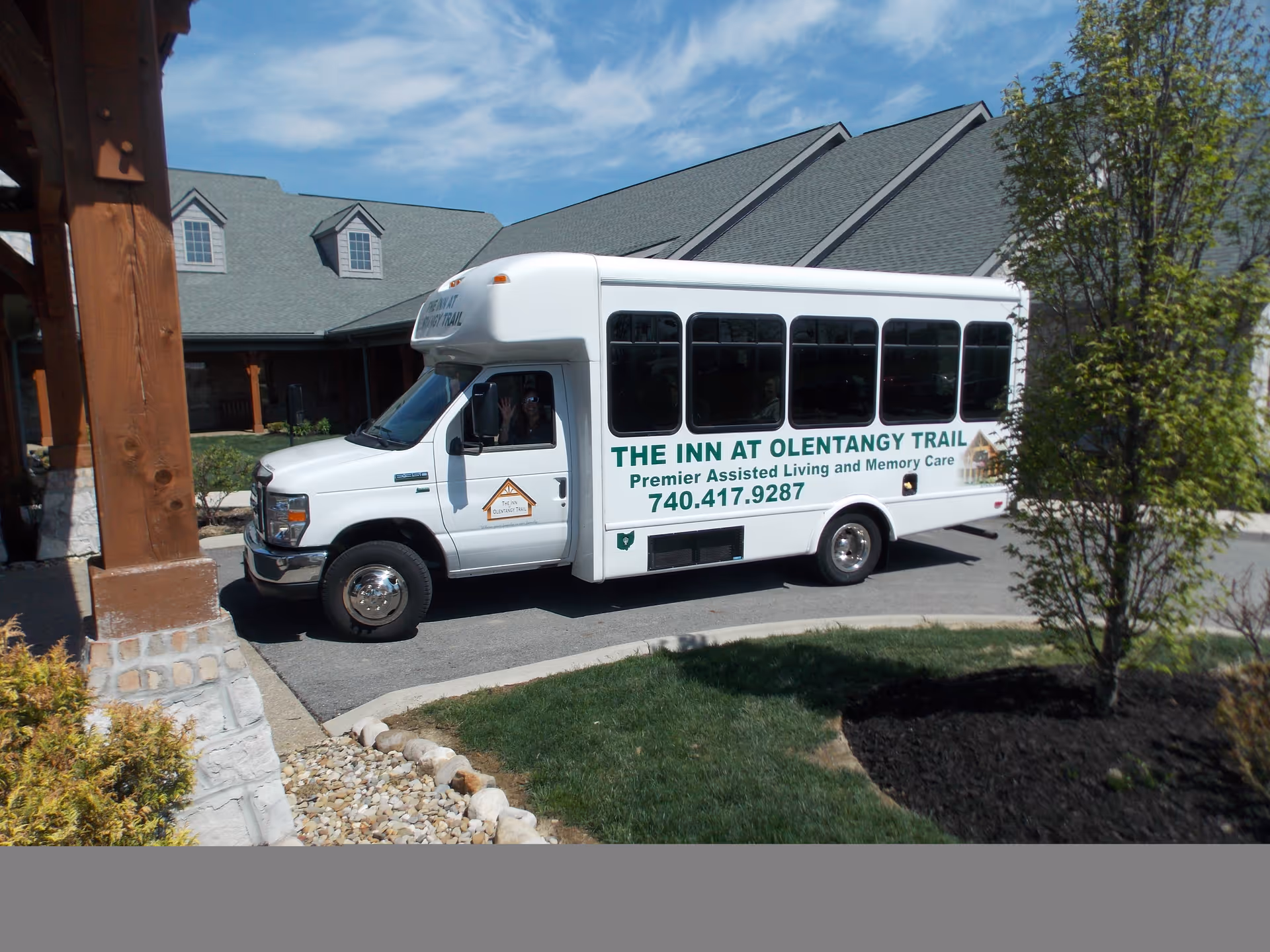 A white shuttle bus labeled 'The Inn at Olentangy Trail' parked at the entrance of a senior living facility.