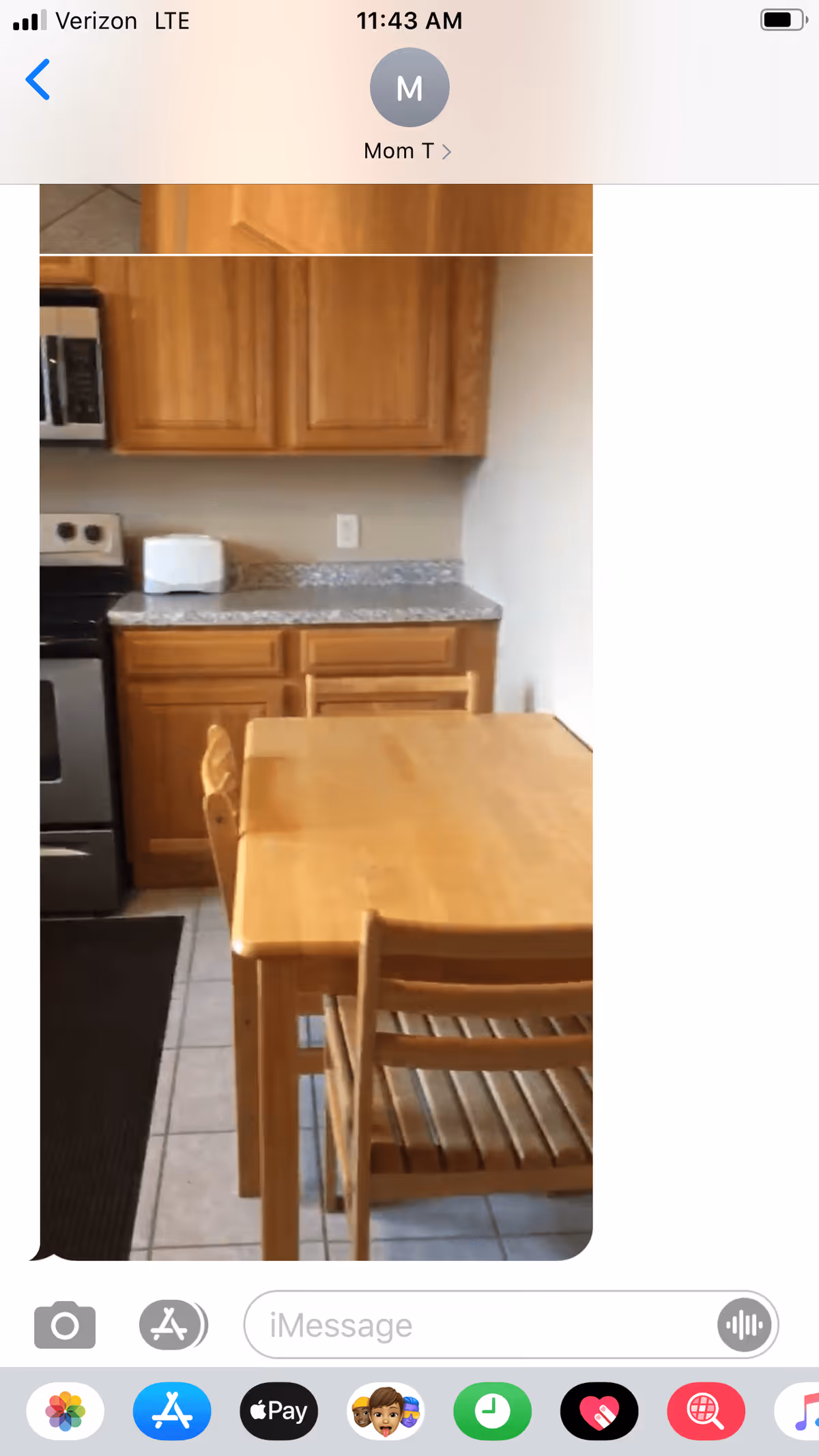 A small kitchen area with wooden cabinets, a granite countertop, a toaster, a stove, and a wooden dining table with two chairs on a tiled floor.