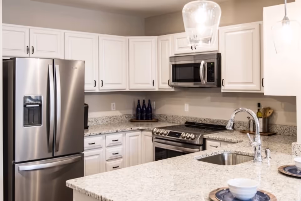 Modern kitchen with stainless steel refrigerator, stove and microwave, white cabinets, and a granite island with sink and place settings.