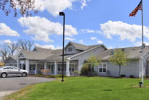 Front exterior of Trustwell Living at Kingsbury Place with parking and a flag.