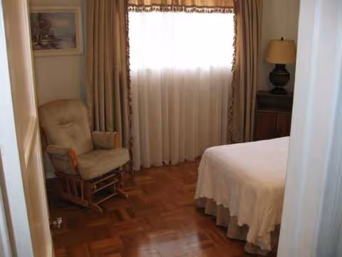 Cozy bedroom featuring a bed, rocking chair, and curtained window.