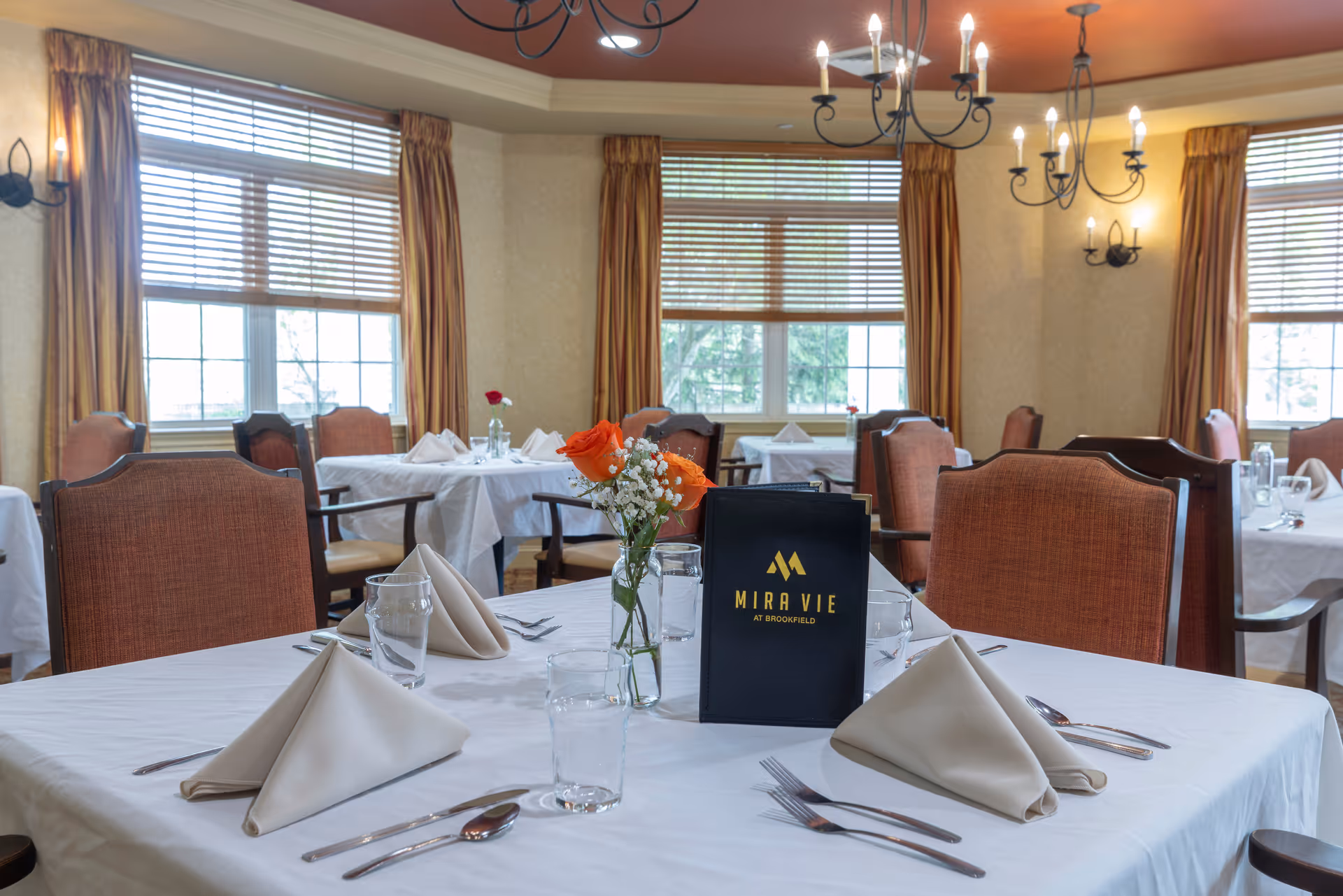 Formal dining room with set tables, folded napkins, glassware and a Mira Vie at Brookfield menu centerpiece.