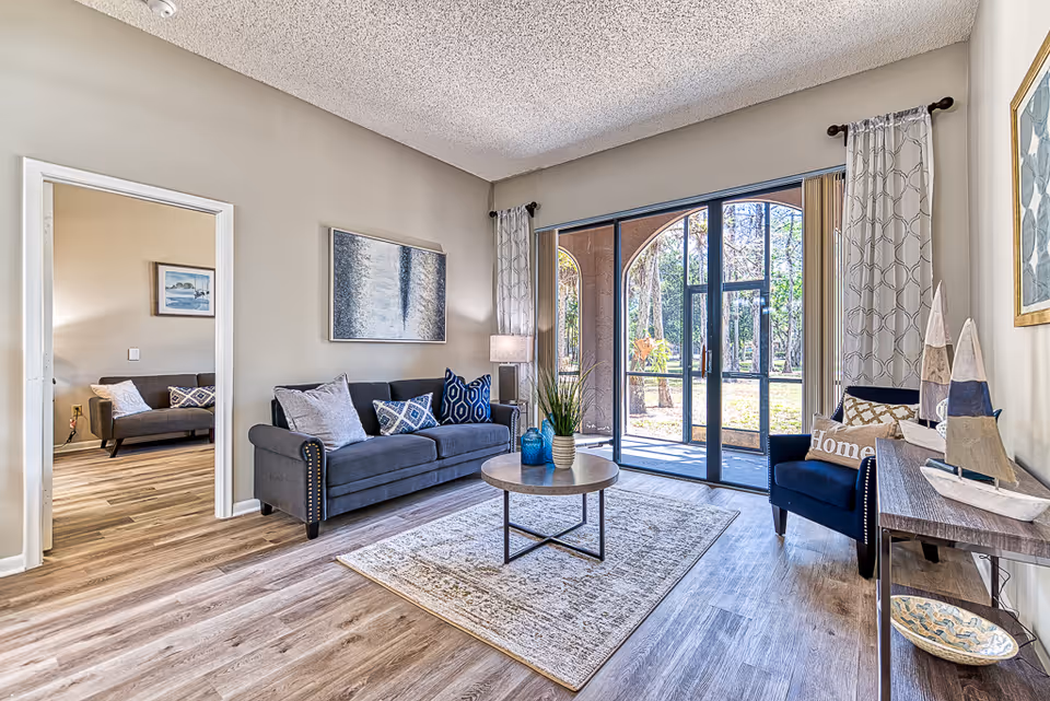 Spacious living room with gray sofas and an armchair around a round coffee table on a rug, large arched glass doors leading outside, and wood-look flooring.
