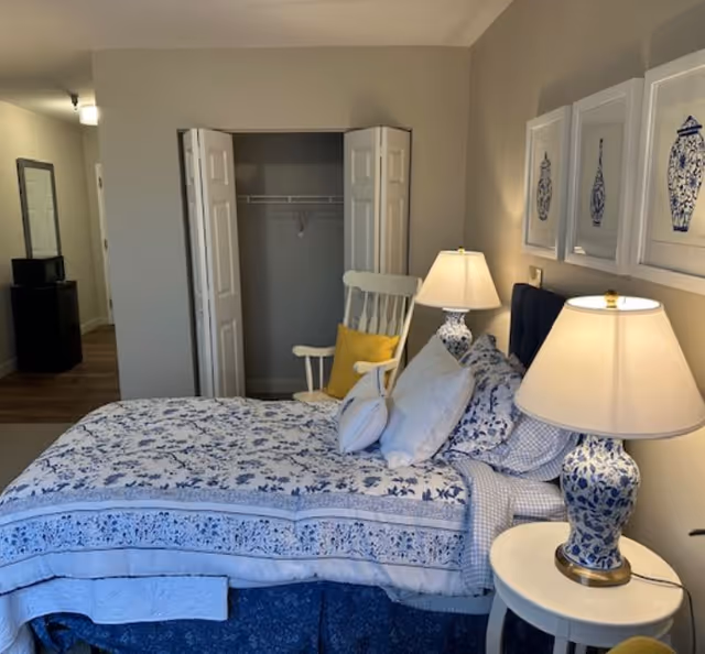 Bedroom with a blue-and-white patterned bed, two bedside lamps, a rocking chair, and an open closet.