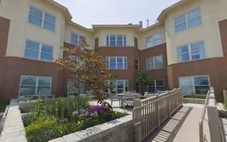 Three-story brick-and-light siding senior living building facing a landscaped central courtyard with raised planters, seating, and an accessible ramp.
