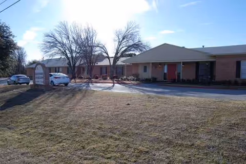 Single-story brick senior living facility with a covered entrance, parking, and leafless trees.
