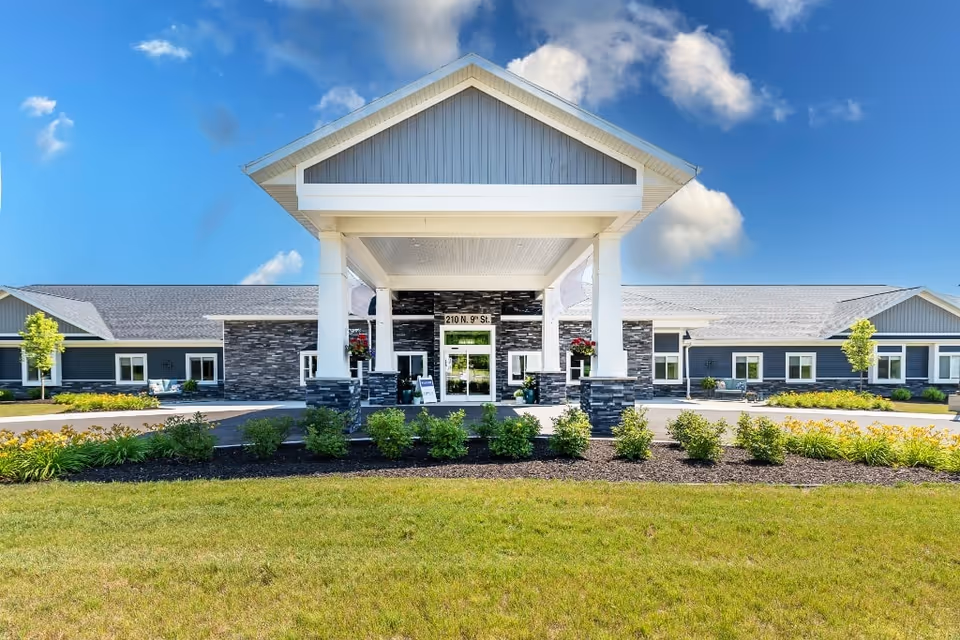 Front entrance of a single-story senior living facility with a covered porte-cochere, stone accents, and landscaped lawn.