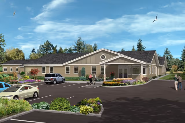 Exterior view of a single-story senior living facility building with a parking lot in front. The building has beige siding, a dark roof, and a covered entrance with columns. There are landscaped flower beds and shrubs around the building and parking area. Several people are walking near the entrance and parking lot. The sky is blue with some clouds and birds flying.