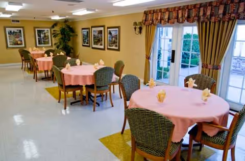 Dining room with pink tablecloths, round tables, wicker chairs, and curtains.