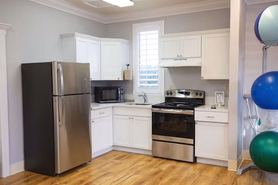 Kitchen area with stainless steel refrigerator and oven, white cabinets, a microwave, and exercise balls visible on the right.