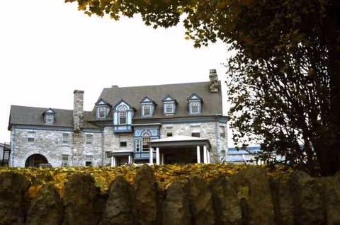 Stone mansion-style senior living facility exterior with a stone fence and autumn leaves.