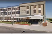 Exterior front view of Beacon Rehabilitation Nursing Center, a multi-story building with a covered entrance, landscaping with flowers and shrubs, and a sidewalk in front.