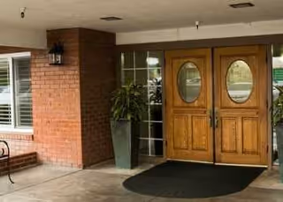 Exterior entrance of a brick building with wooden double doors and potted plants.