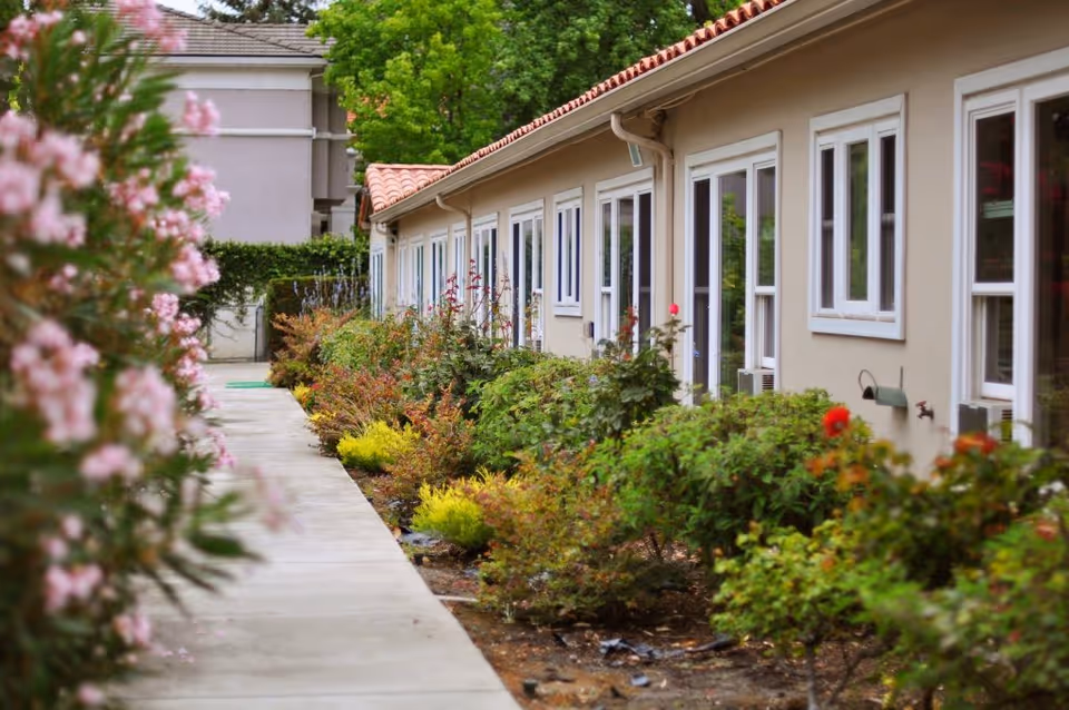 A landscaped sidewalk runs alongside a one-story building with multiple windows and doors.