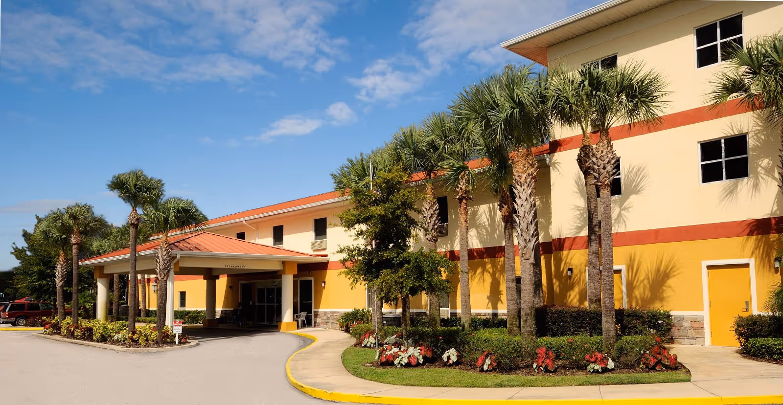 Sunlit exterior view of Balmoral Assisted Living building with palm trees and entrance canopy.