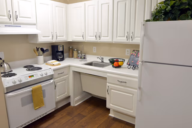 Small U-shaped kitchen with white cabinets, electric stove, sink, refrigerator, and wood floors.